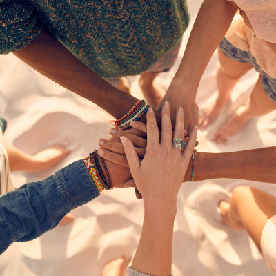 Image of a a group of women's hands together on a beach